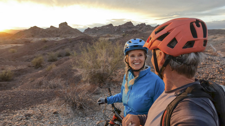 Mature mountain biking couple pause on desert trail at sunrise retirees